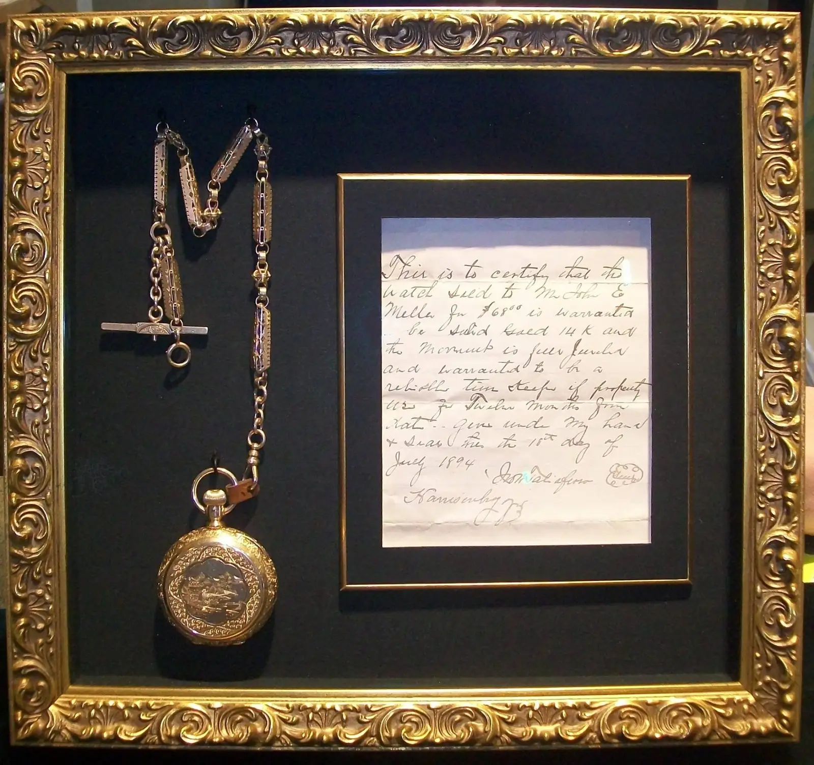 Ornate gold frame holding a gold pocket watch on a chain next to a handwritten document